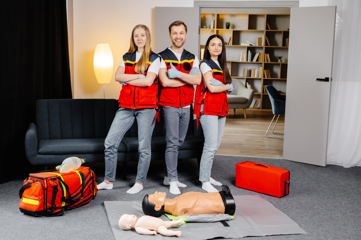Three LifeLine instructors in red vests with CPR manikins and training bags